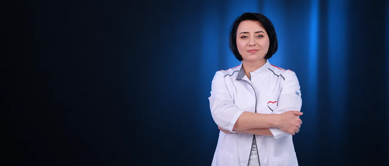 Dr. Hasmik Badalyan in a white medical coat, arms crossed, blue backdrop