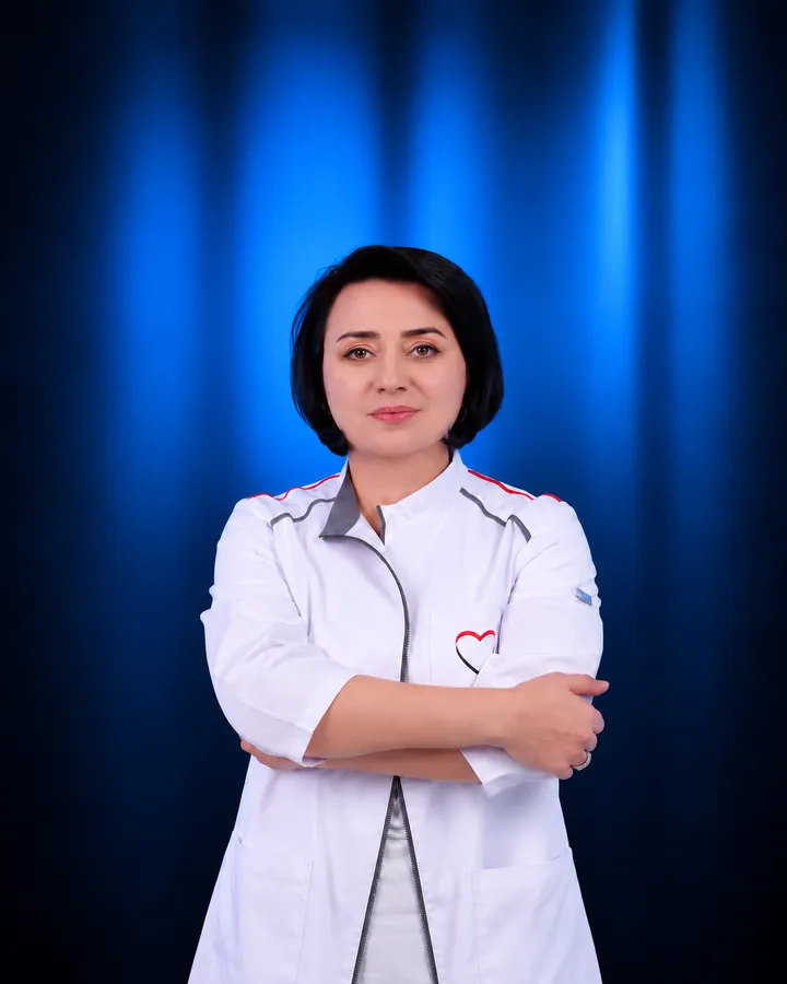 Dr. Hasmik Badalyan in a white medical coat, arms crossed, blue backdrop